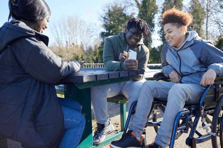 Three young people smiling outdoors around a picnic bench